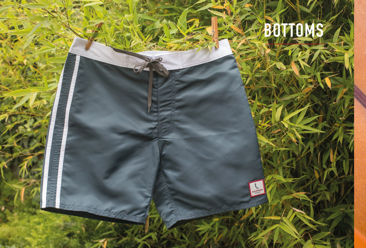 Classic style board shorts hanging in front of bamboo plant.
