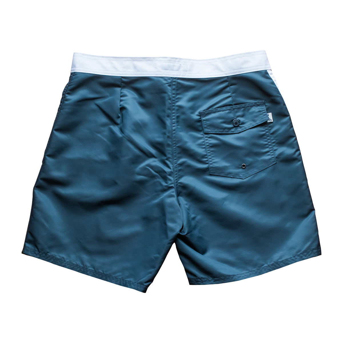 Back view of vintage style surf trunks in blue with white trim and white stripes on side. Material is a durable satin nylon. Severson icon label on back pocket.