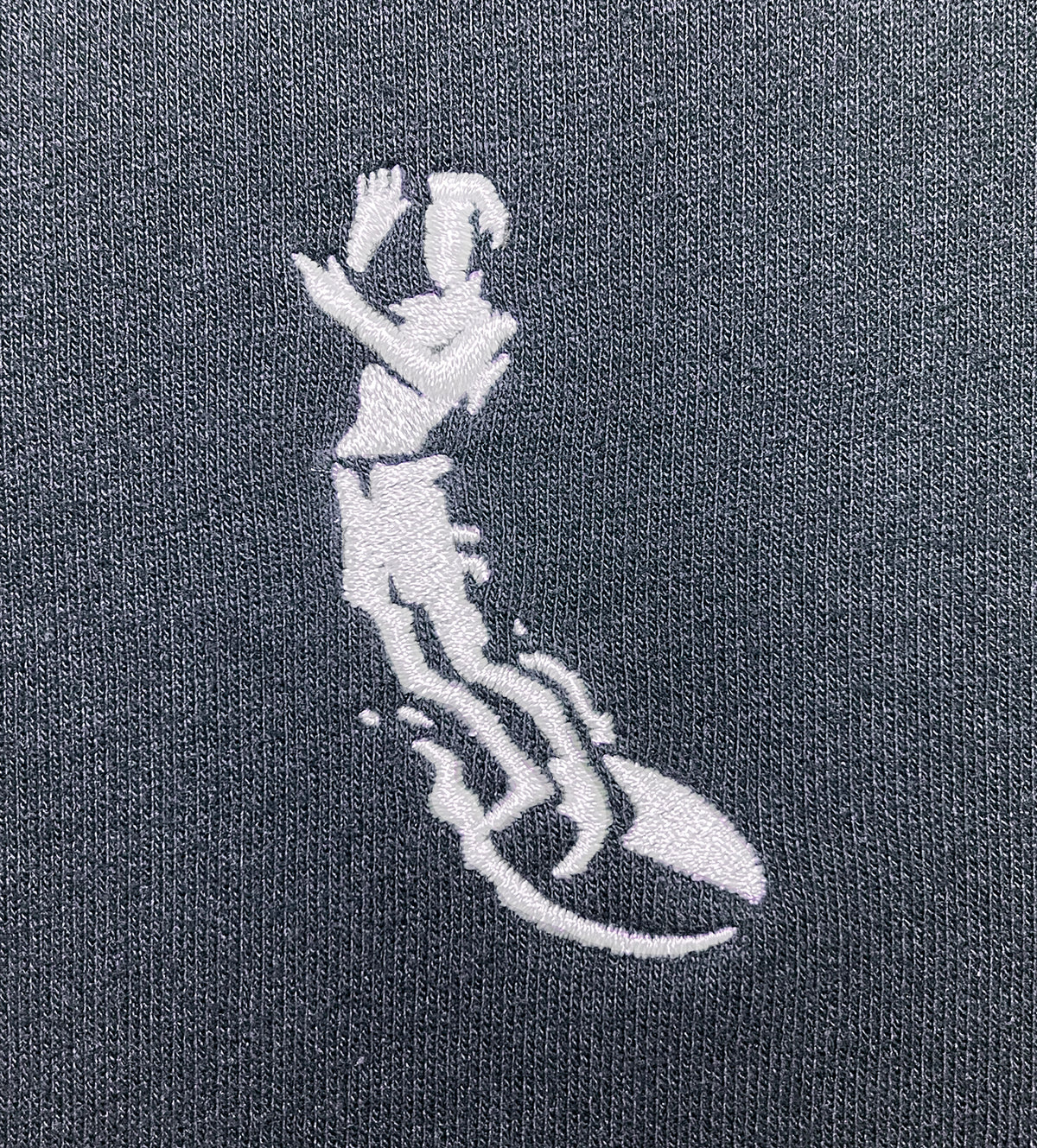 close up of Small Left chest embroidery of severson surfer icon in white.