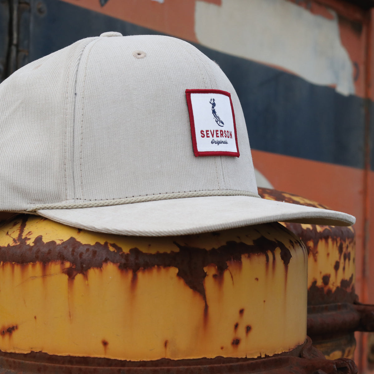 Photo of Mens snapback corduroy hat in khaki with Severson Originals logo in red, white and blue square patch. Rusty truck in background.