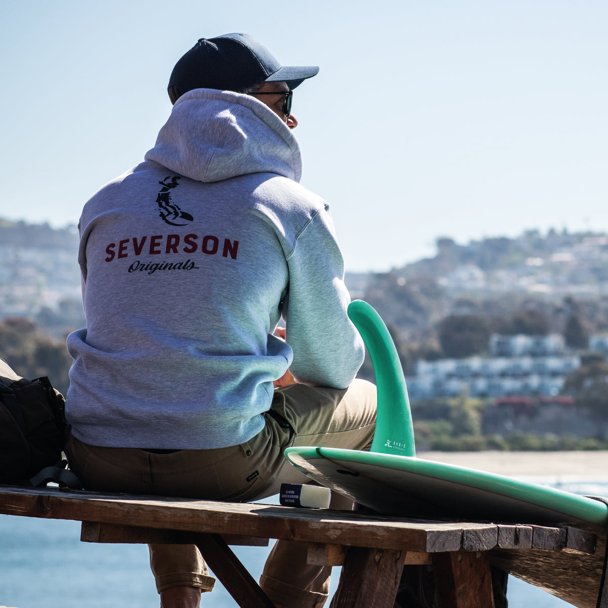 Surfer checking to the waves at Doheny Beach in Dana Point, with longboard on bench. wearing the Soul Arch hoodie in grey heather.